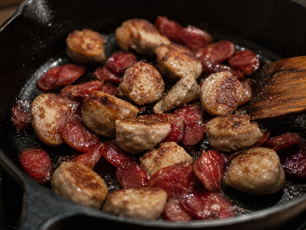Sliced lap cheong Chinese sausage and halved meatballs pan-fried in a cast-iron skillet